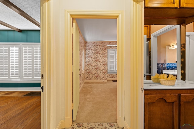 hallway with a textured ceiling, carpet floors, baseboards, beam ceiling, and wallpapered walls