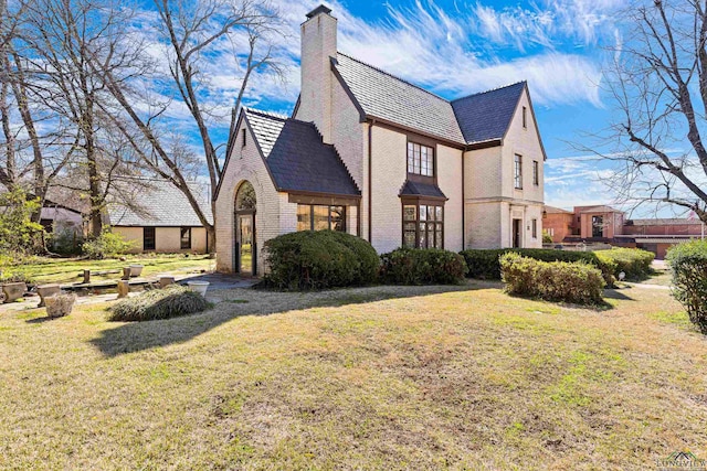 view of side of home featuring a high end roof, brick siding, a lawn, and a chimney