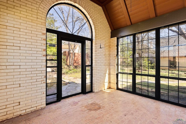 interior space featuring wood ceiling, brick wall, beamed ceiling, brick floor, and high vaulted ceiling