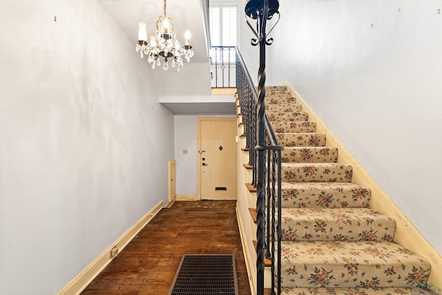 staircase with baseboards, visible vents, a towering ceiling, wood finished floors, and a notable chandelier