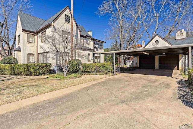 view of home's exterior featuring an attached carport, a garage, brick siding, driveway, and a chimney