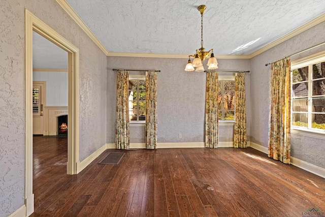 unfurnished dining area with crown molding, an inviting chandelier, a lit fireplace, baseboards, and hardwood / wood-style flooring