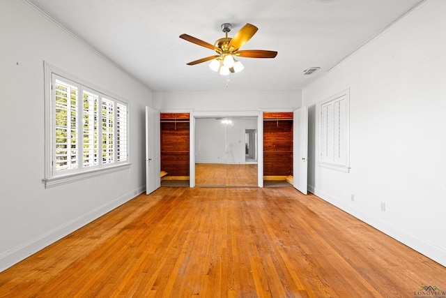 unfurnished bedroom with visible vents, baseboards, hardwood / wood-style flooring, crown molding, and multiple closets