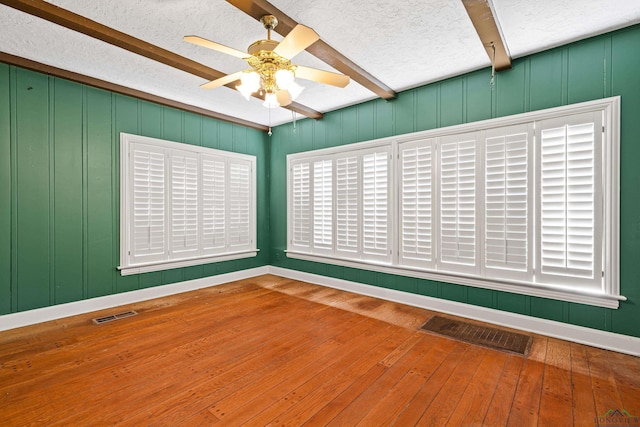 empty room featuring a textured ceiling, beamed ceiling, wood-type flooring, and visible vents