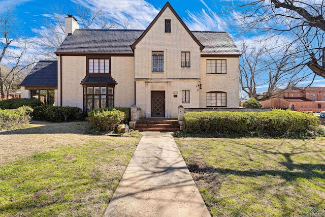 tudor home featuring a chimney, a front lawn, and brick siding