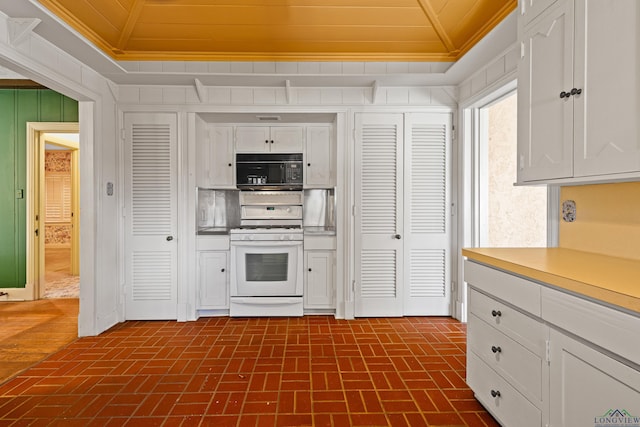 kitchen with brick floor, black microwave, white cabinets, and white gas range