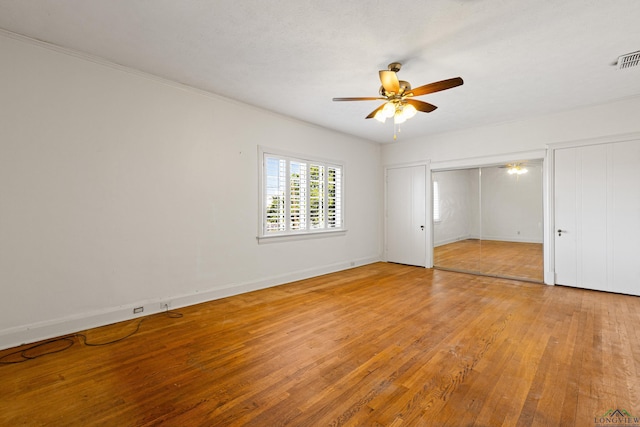 unfurnished bedroom with light wood-style flooring, visible vents, a ceiling fan, baseboards, and two closets