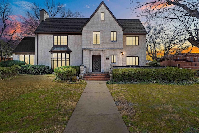 tudor house with a chimney, a front lawn, and brick siding