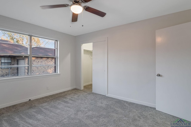 unfurnished bedroom with carpet floors, a closet, a spacious closet, and ceiling fan