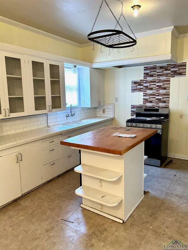 kitchen with sink, butcher block counters, white cabinets, a kitchen island, and gas range