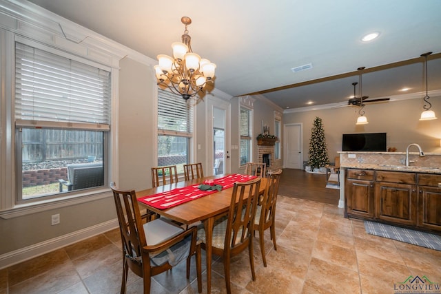 dining room with ceiling fan with notable chandelier, crown molding, sink, and a brick fireplace