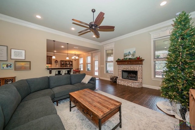 living room with a brick fireplace, hardwood / wood-style floors, ceiling fan with notable chandelier, and ornamental molding