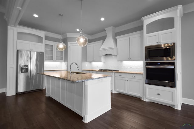 kitchen with premium range hood, stainless steel appliances, sink, hanging light fixtures, and an island with sink