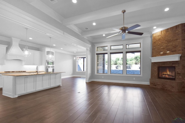 unfurnished living room with sink, ceiling fan, a fireplace, beam ceiling, and dark hardwood / wood-style flooring