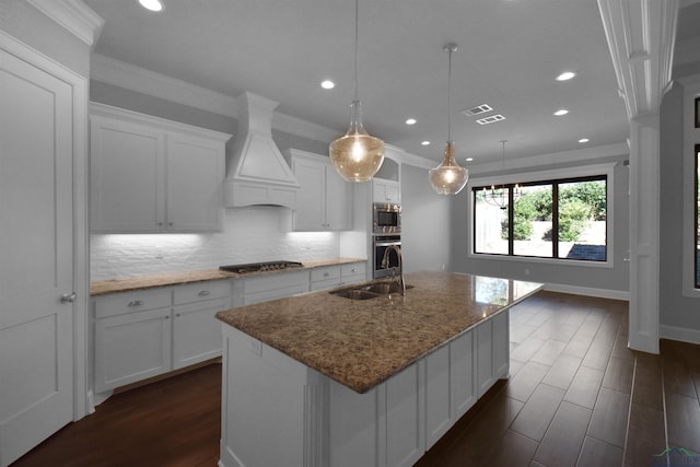 kitchen with pendant lighting, a kitchen island with sink, white cabinets, light stone countertops, and custom range hood