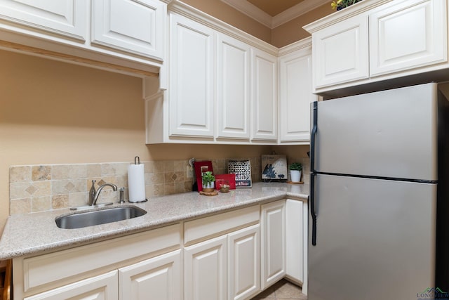 kitchen featuring sink, white cabinetry, ornamental molding, and stainless steel refrigerator