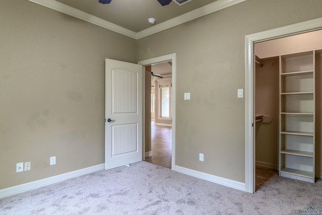 unfurnished bedroom with crown molding, a walk in closet, light carpet, and a closet