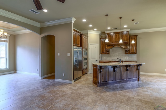 kitchen with appliances with stainless steel finishes, decorative backsplash, hanging light fixtures, light stone countertops, and a center island with sink