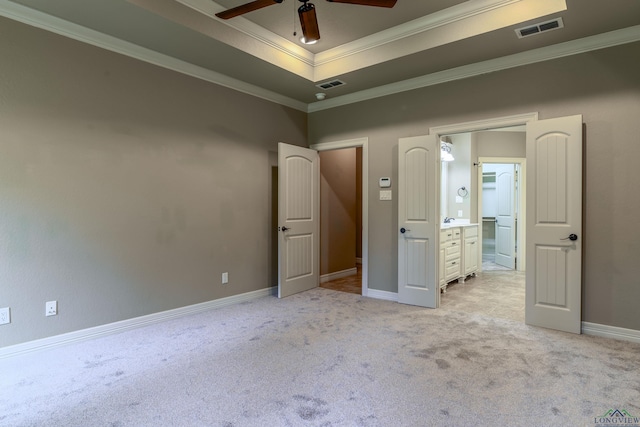 unfurnished bedroom featuring ceiling fan, connected bathroom, a tray ceiling, ornamental molding, and light colored carpet