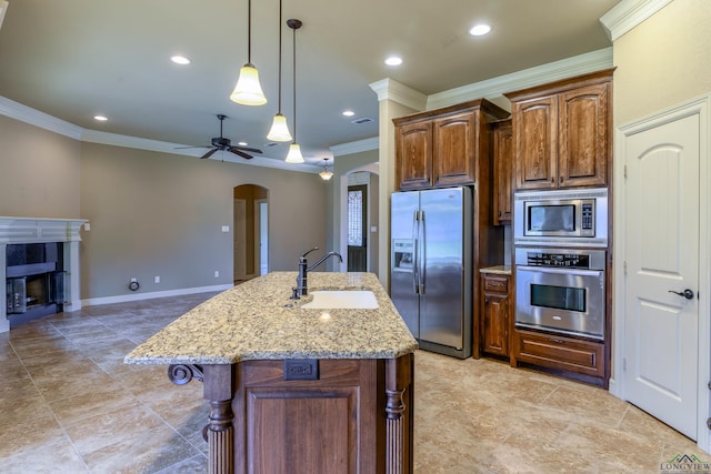 kitchen featuring appliances with stainless steel finishes, an island with sink, sink, a tiled fireplace, and light stone countertops