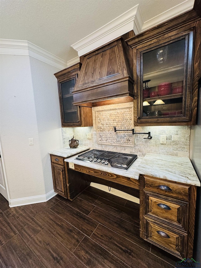 kitchen featuring dark brown cabinetry, custom exhaust hood, decorative backsplash, stainless steel gas cooktop, and ornamental molding