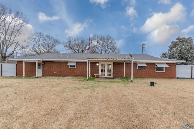 back of property with french doors, brick siding, a lawn, and fence