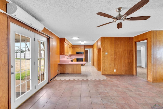 kitchen with a peninsula, a sink, light countertops, wood walls, and under cabinet range hood