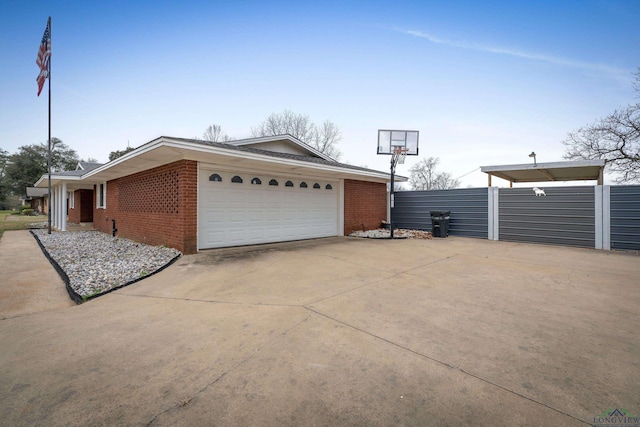 view of side of home featuring a garage, brick siding, driveway, and fence