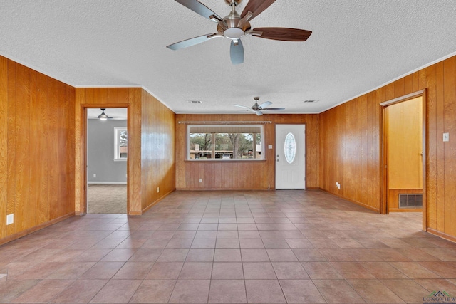 unfurnished living room featuring visible vents, wooden walls, tile patterned flooring, and a textured ceiling