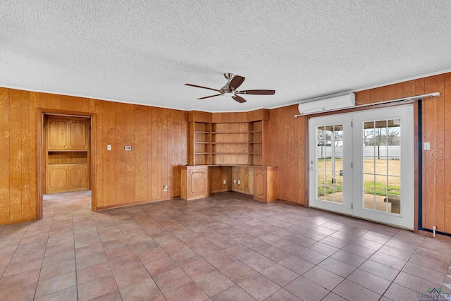 empty room with wooden walls, built in shelves, a wall mounted air conditioner, built in desk, and a textured ceiling