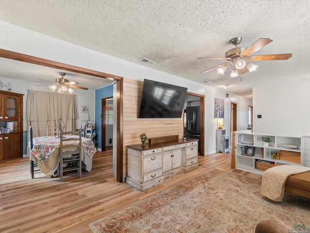 living room featuring ceiling fan, wood walls, a textured ceiling, and light hardwood / wood-style flooring