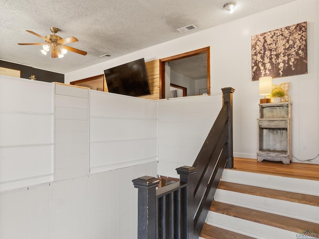 stairway with hardwood / wood-style flooring, ceiling fan, and a textured ceiling