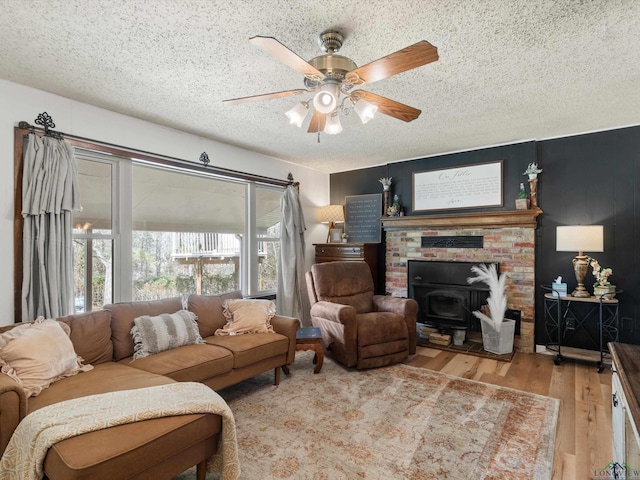 living room featuring ceiling fan, a textured ceiling, light hardwood / wood-style flooring, and a wood stove