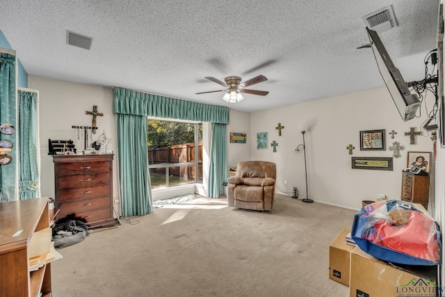 living area featuring light carpet, ceiling fan, and a textured ceiling