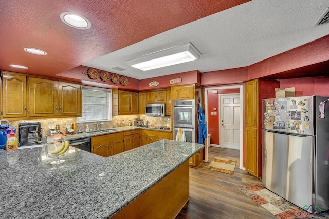 kitchen featuring sink, dark hardwood / wood-style flooring, dark stone countertops, a textured ceiling, and appliances with stainless steel finishes