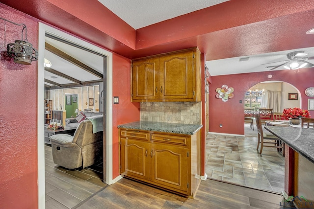 kitchen featuring decorative backsplash, ceiling fan with notable chandelier, a textured ceiling, dark wood-type flooring, and beam ceiling