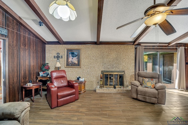 living room featuring beamed ceiling, a textured ceiling, a brick fireplace, and ceiling fan