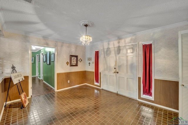 entrance foyer with wooden walls, a chandelier, a textured ceiling, and ornamental molding