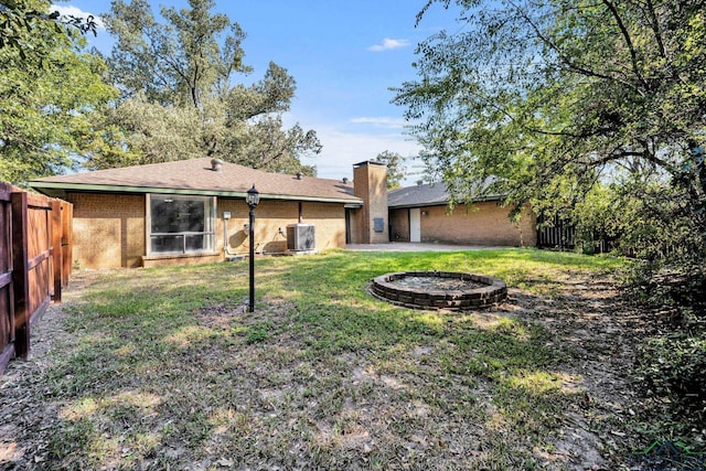 rear view of property with a lawn, central air condition unit, and an outdoor fire pit