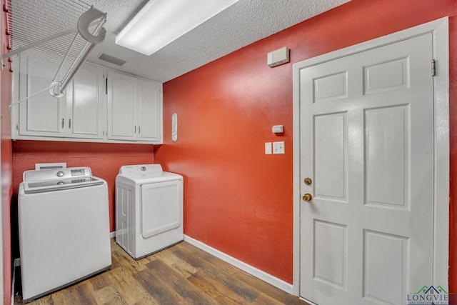 clothes washing area with dark hardwood / wood-style floors, cabinets, a textured ceiling, and washing machine and clothes dryer