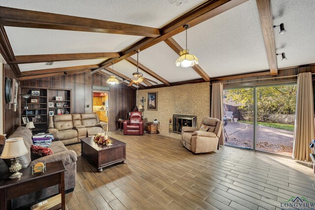 living room with a textured ceiling, ceiling fan, a fireplace, vaulted ceiling with beams, and wood walls