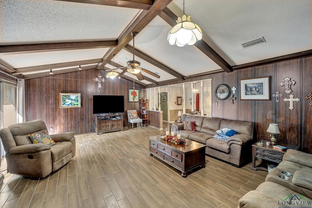 living room with lofted ceiling with beams, wooden walls, ceiling fan, a textured ceiling, and light hardwood / wood-style floors