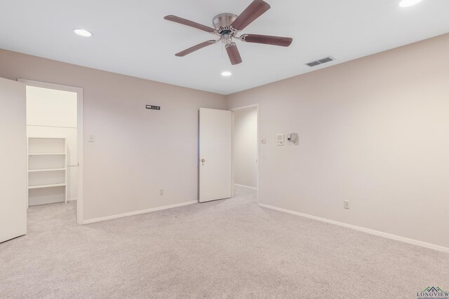 unfurnished bedroom with ceiling fan, a spacious closet, light carpet, and a closet