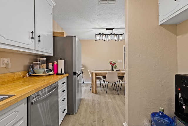 kitchen with stainless steel appliances, butcher block counters, white cabinets, and a textured ceiling