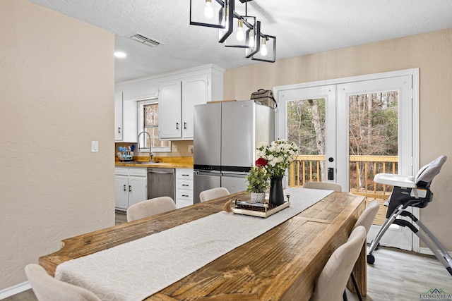 dining space with sink, light hardwood / wood-style flooring, french doors, and a textured ceiling