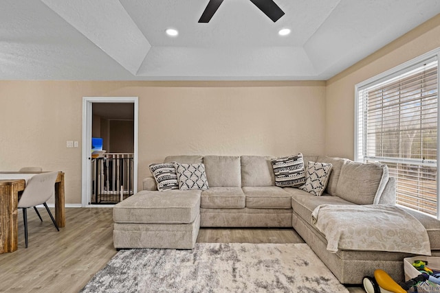 living room featuring ceiling fan, light wood-type flooring, and a tray ceiling