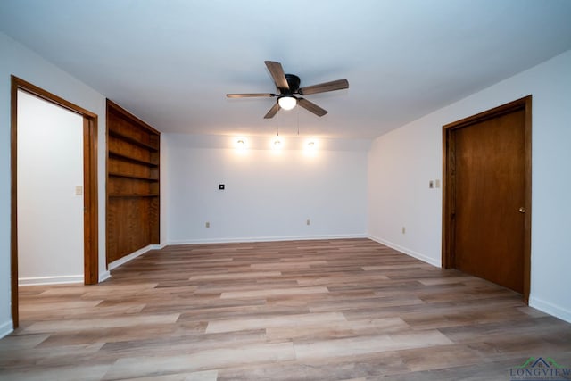 unfurnished room with ceiling fan, light wood finished floors, built in features, and baseboards