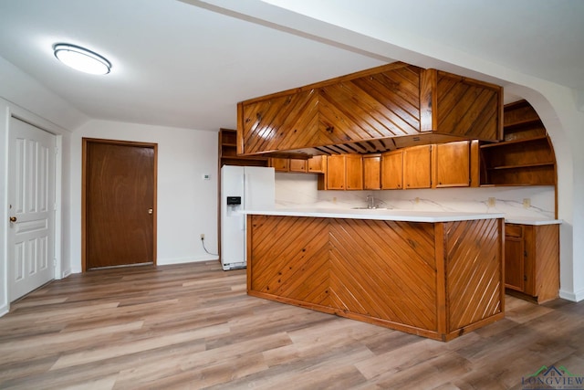 kitchen with light wood finished floors, brown cabinetry, light countertops, white fridge with ice dispenser, and open shelves