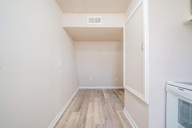 interior space featuring a textured ceiling, light wood finished floors, visible vents, and baseboards