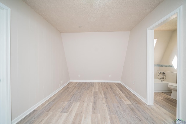 bonus room with a textured ceiling, light wood-type flooring, and baseboards